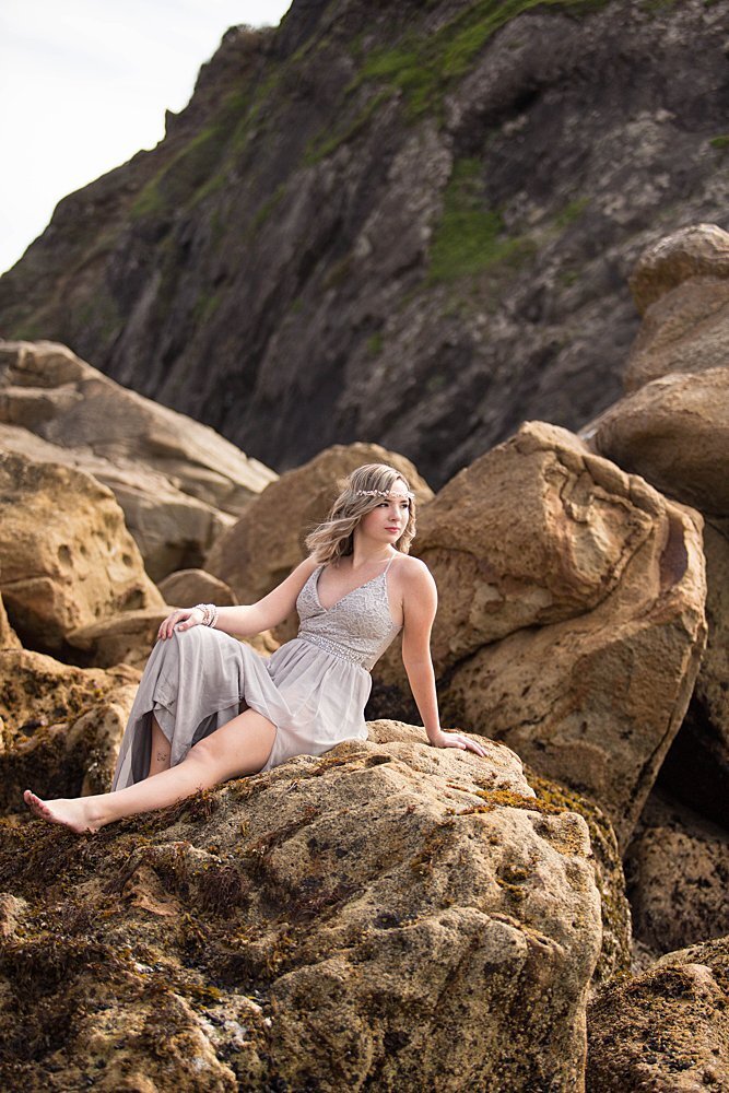 senior girl in dress sitting on rocks on the beach