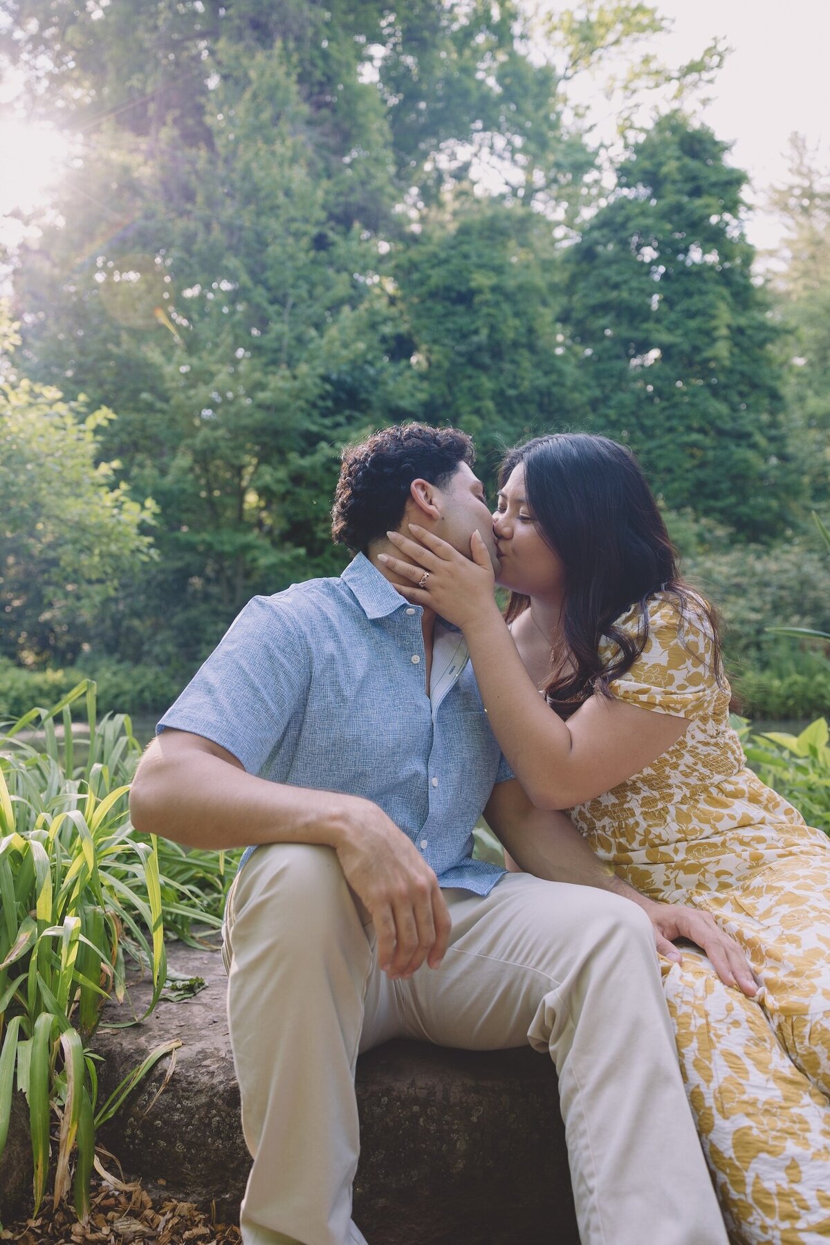 Couple kissing on a garden path with tall greenery behind them.
