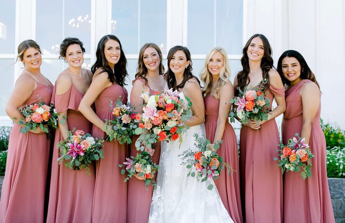 Bride with bridesmaids in mauve dresses holding bright bouquets | Austin wedding party hair and makeup services