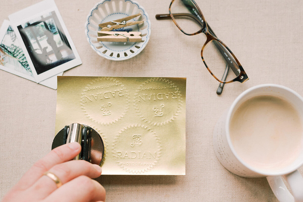 Old family photos, glasses, a branded stamp, and cup of coffee sit atop a table