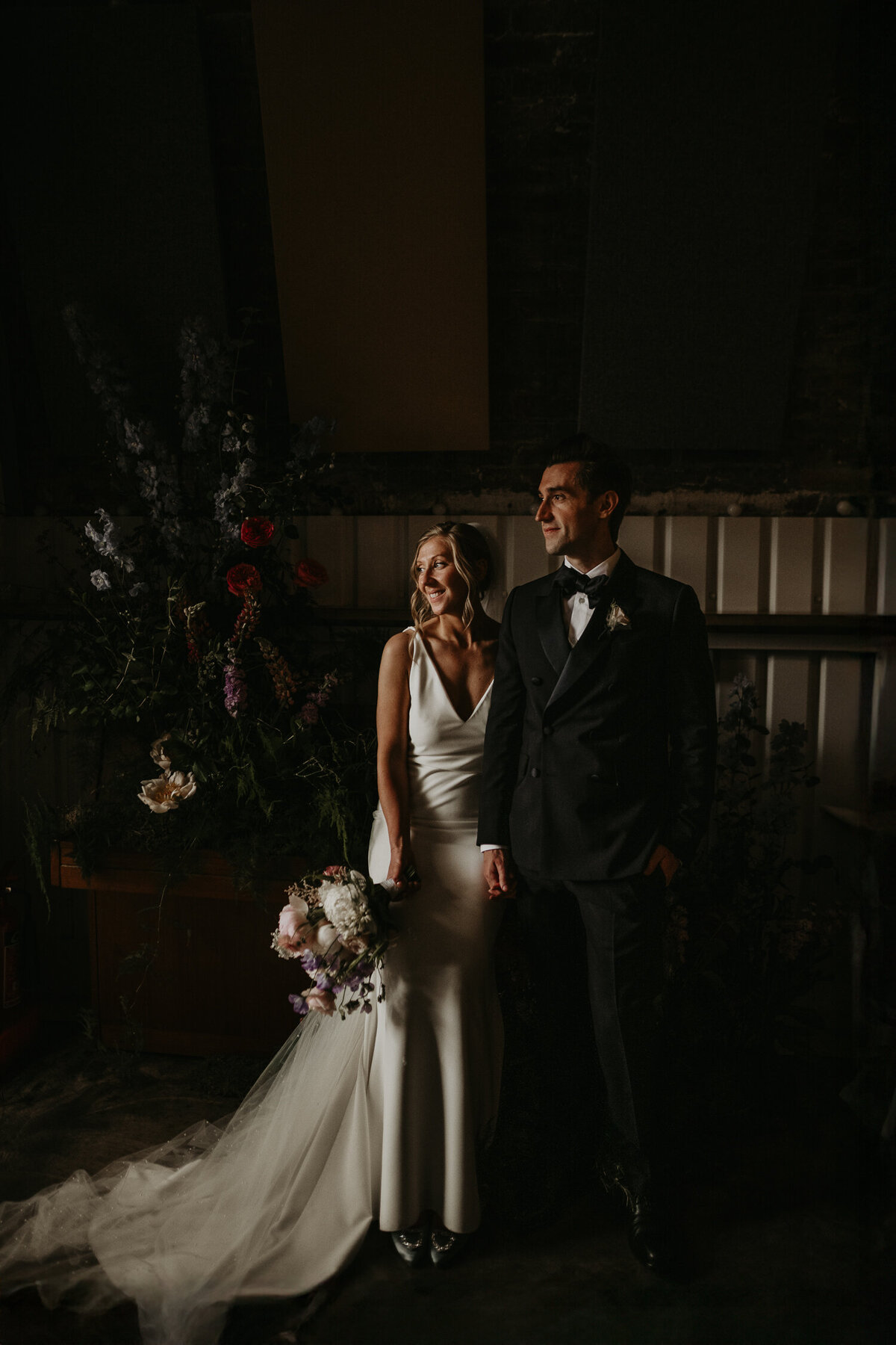 A bride and groom resting next to a piano covered din flowers at AMP Studios in London 