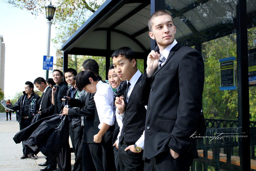 Ten men in suits waiting at the bus stop looking suave