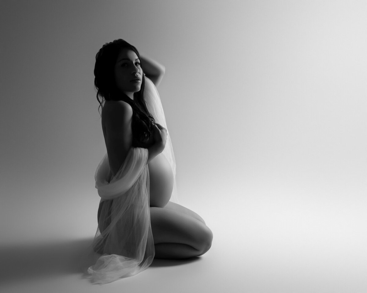 Artistic black and white maternity silhouette of pregnant woman kneeling in studio photography session