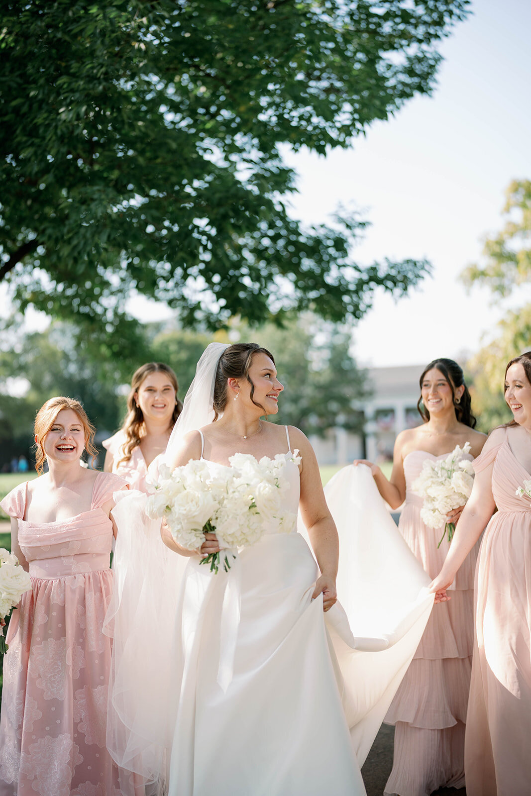 Bride walking with her bridesmaids outside Martha-Mary Chapel in Dearborn Michigan during a September wedding, soft pink bridesmaid dresses, candid wedding party moment.
