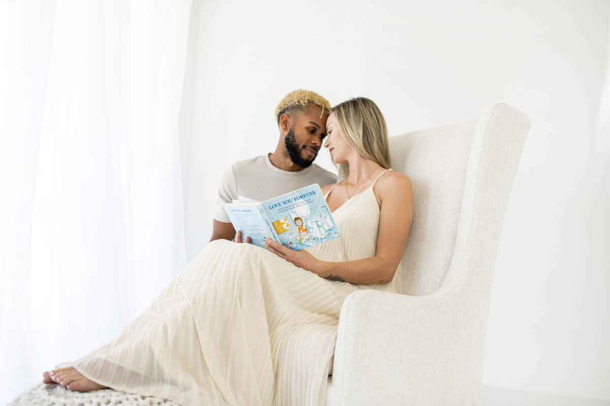 sweet couple reading a classic children's book to their newborn in a rocking chair in oklahoma city
