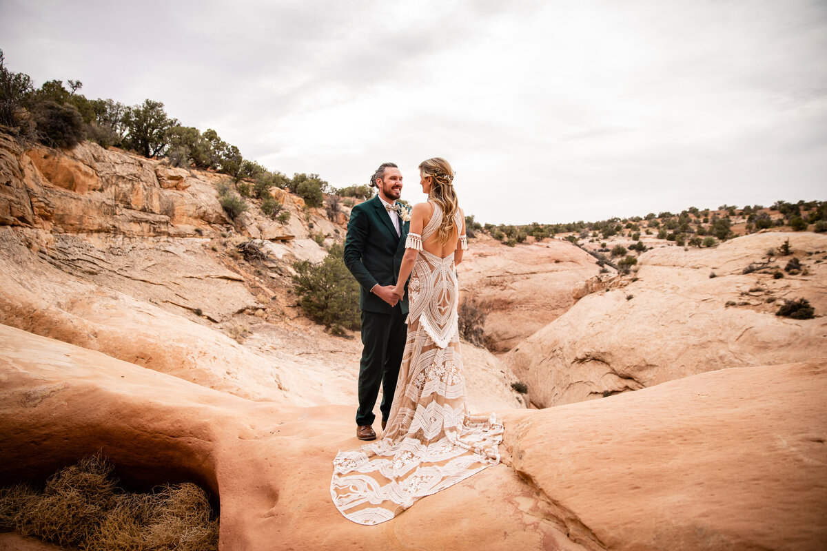 Couple eloping in Moab stand above a canyon holding hands