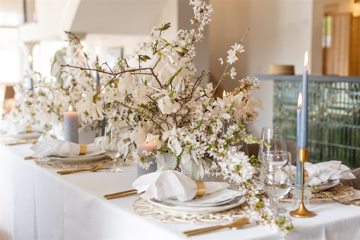 Beautiful table setting with large white floral design, white napkins, and gold details.