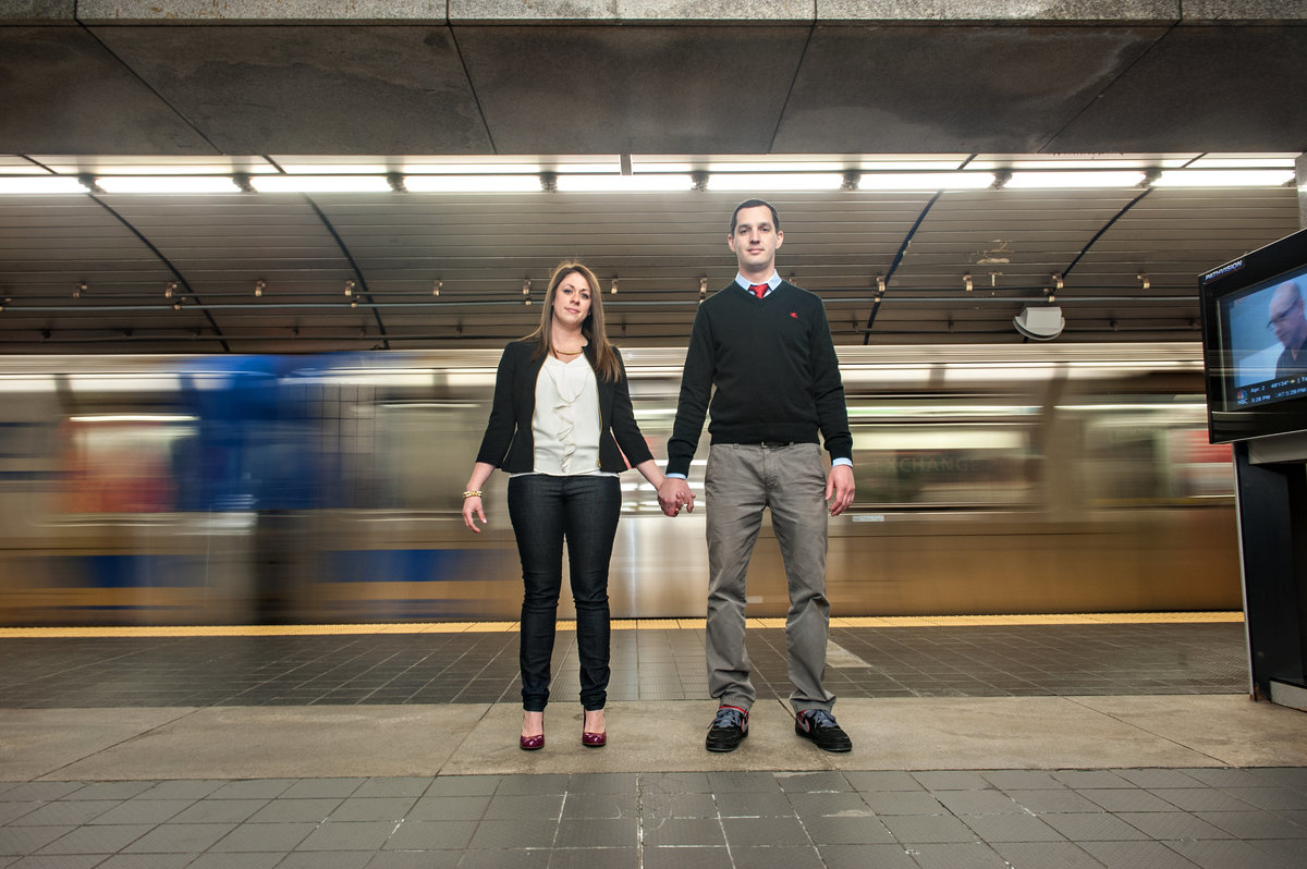 A couple hold hands in front of a moving nyc subway train.