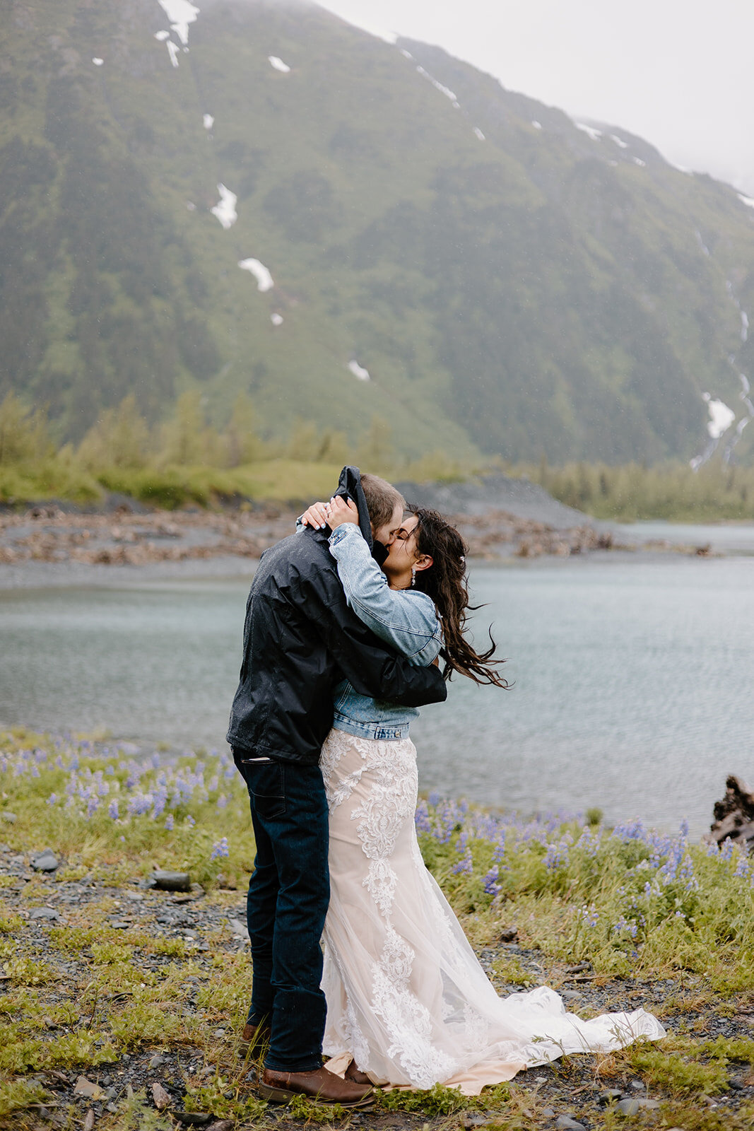 Elopement couple shares kiss by misty Alaska lake and mountain.