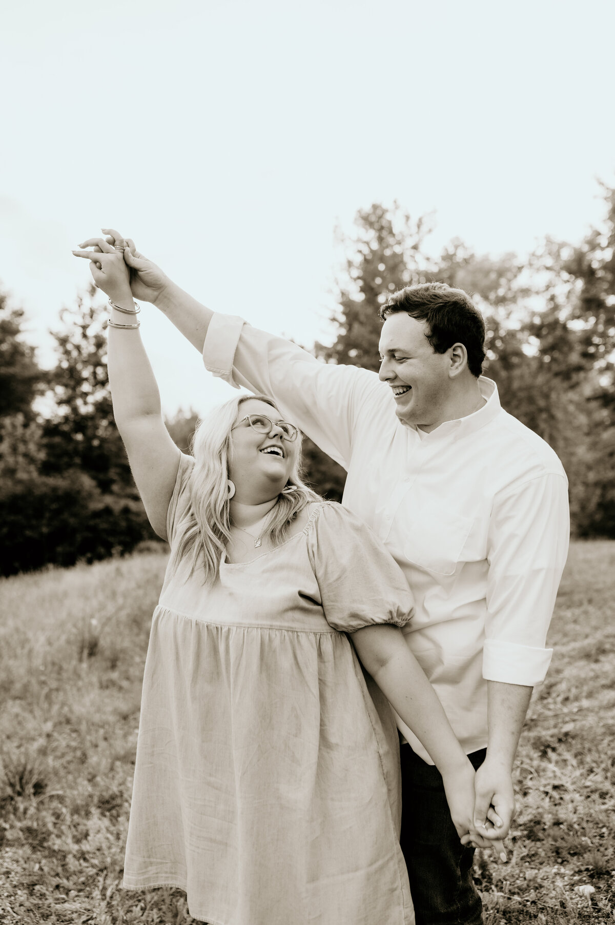 black and white engagement photography with man and woman dancing in a field together as the woman looks back at the man as they smile captured by little rock ar engagement photographer
