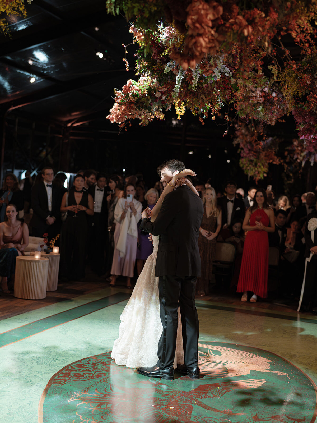 Interacting and sculptural floral clouds hang over the dance floor and bars of this fall wedding reception in Tennessee. Clear top tent build out for fall wedding reception in Tennessee hills.  Product clustered floral clouds in a tasteful fall color palette of copper, ruby, gold, burgundy, rust, and lavender. Orchids, bittersweet berries, butterfly ranunculus, and tulips are highlighted. Unique floral design with flower forward large scale installations. Design by Rosemary & Finch Floral Design in Nashville, TN.