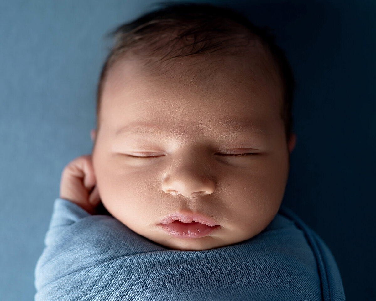 A closeup image of a newborn baby sleeping in a blue swaddle
