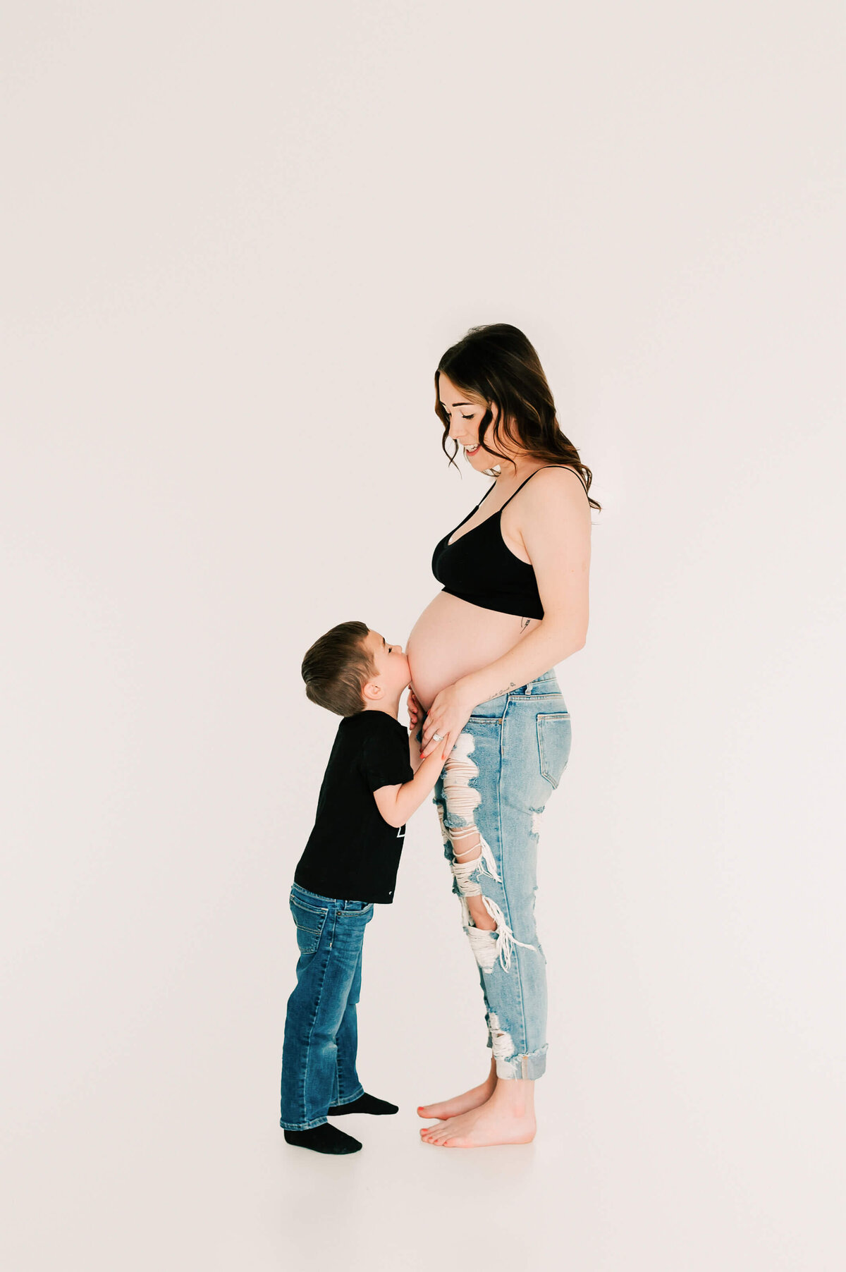 toddler son kissing pregnant mom belly during studio maternity photography in Springfield MO