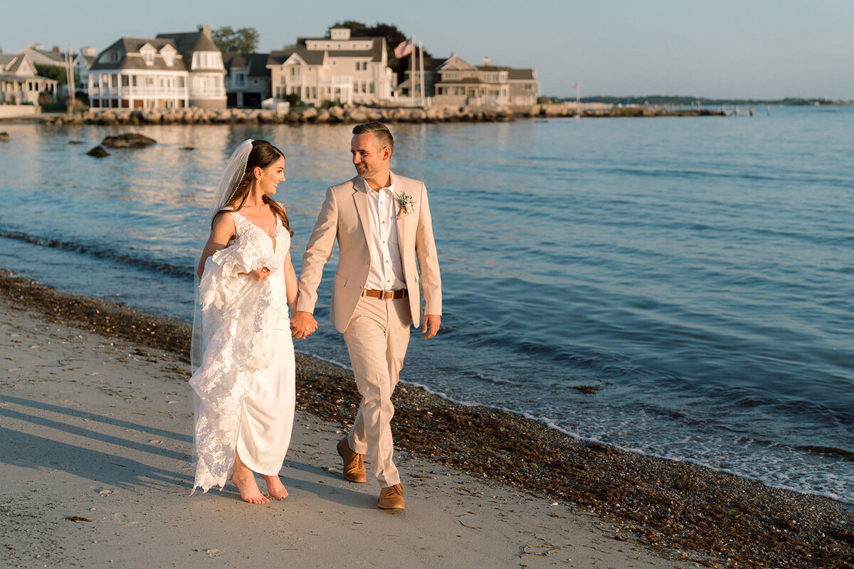 A romantic stroll by the water's edge, with the bride and groom walking side by side on a quiet beach at dusk.
