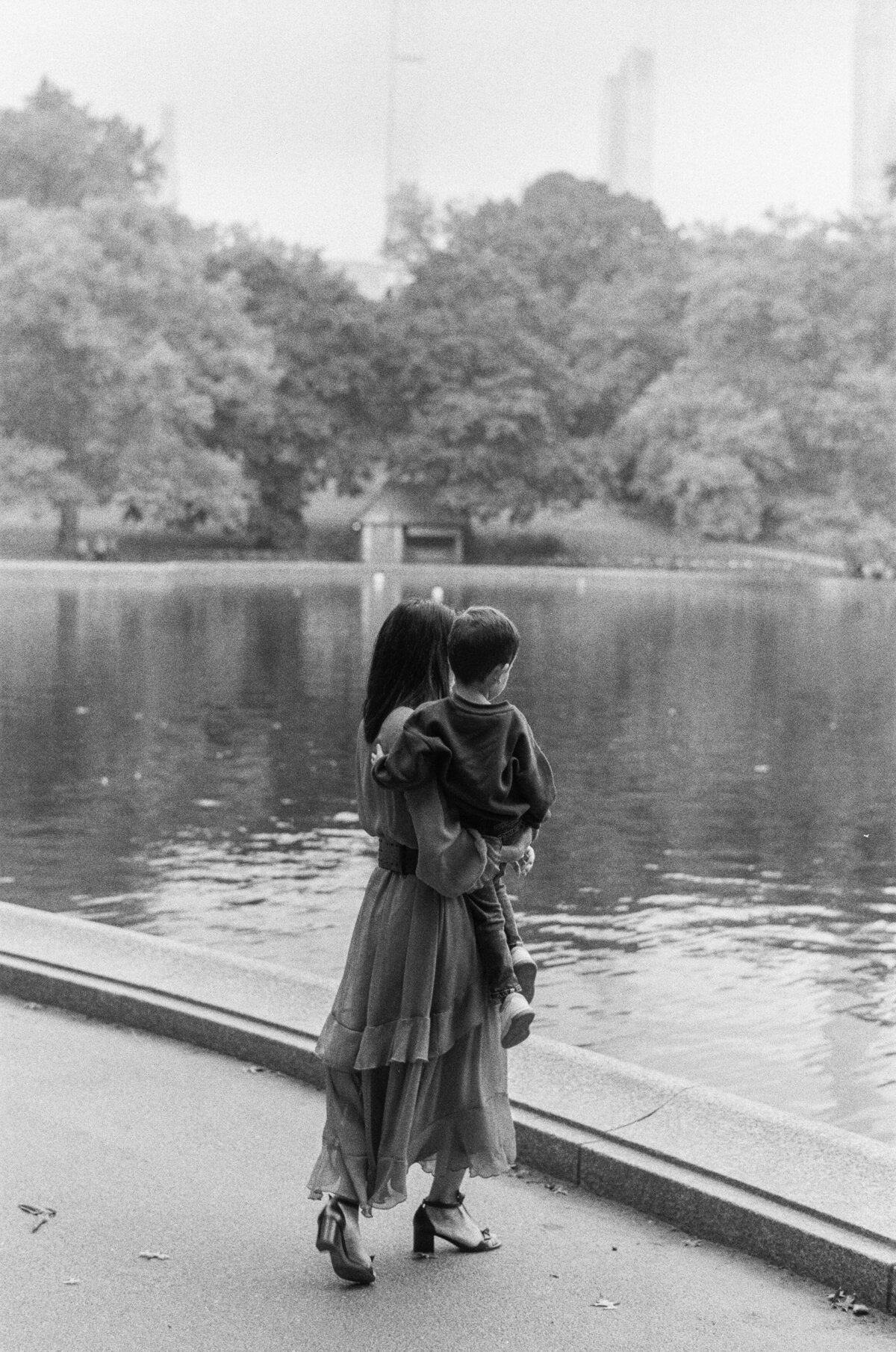 Woman holds her son on her hip while they look at the water