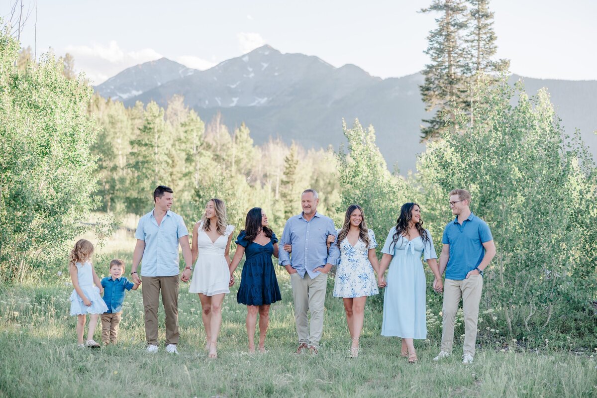 A large family walks in the forest holding hands and smiling at each other in summer