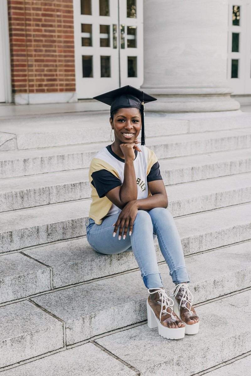 Vanderbilt University graduate sitting on the steps of Wyatt Center wearing light-colored jeans and a yellow, black, and white Vanderbilt t-shirt