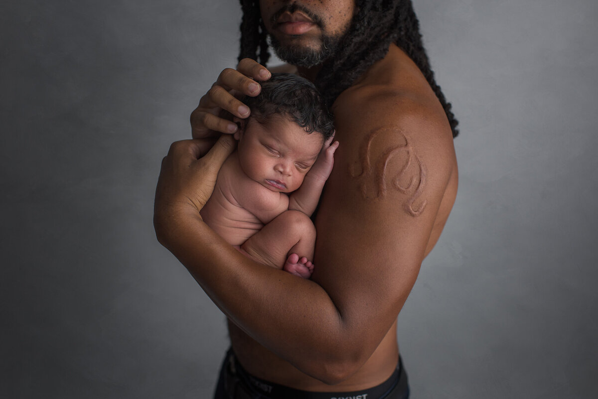a father holding baby in a family photography session dark grey background
