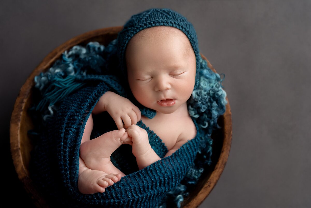 Newborn photography wellington studio poses baby boy in a bowl with teal color scheme.