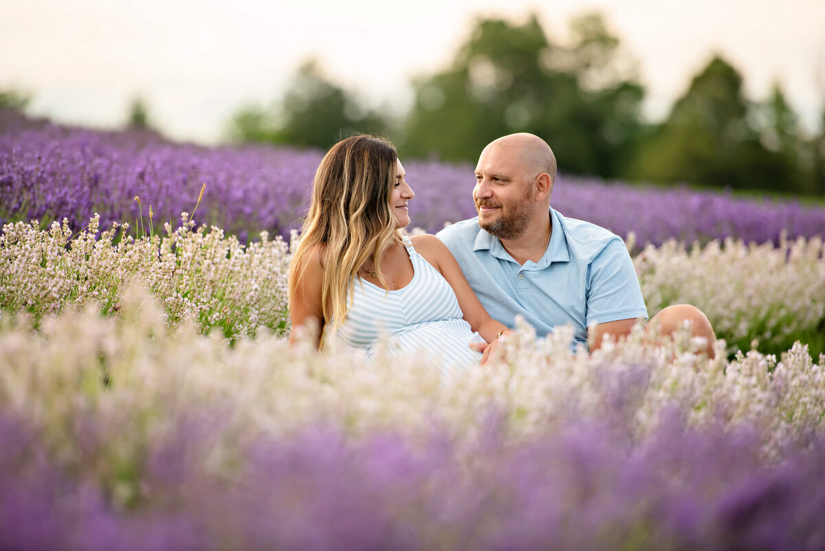 pregnant woman and her husband sitting in a field of lavender for her outdoor maternity photography session in Burlington, ON