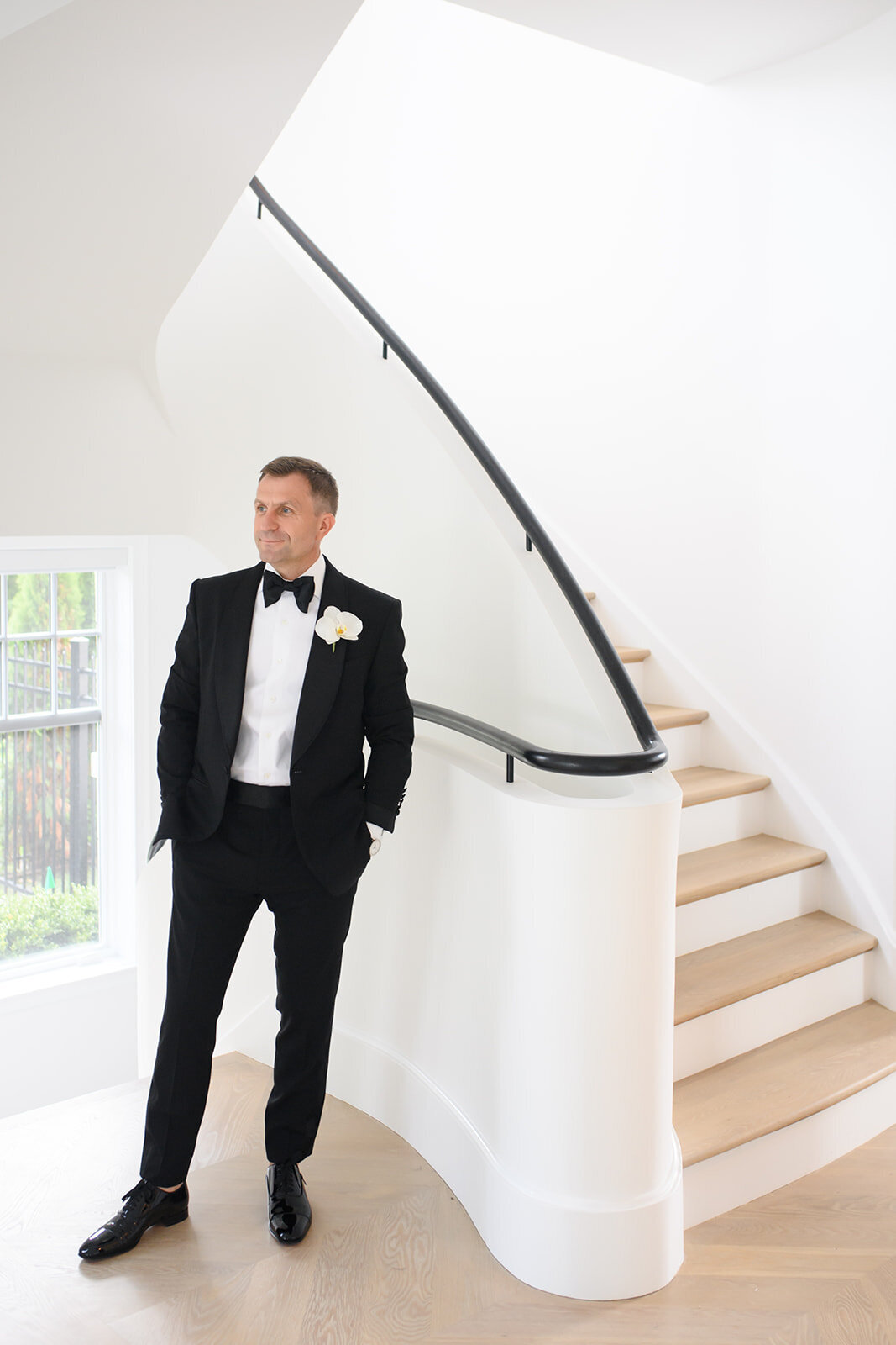 Groom in full attire posing by a staircase.