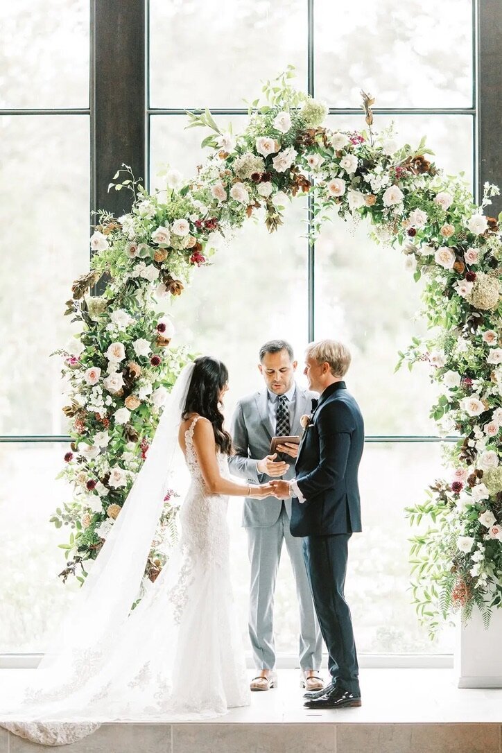 Wedding Photography, bride and groom standing under a large floral archway during the ceremony