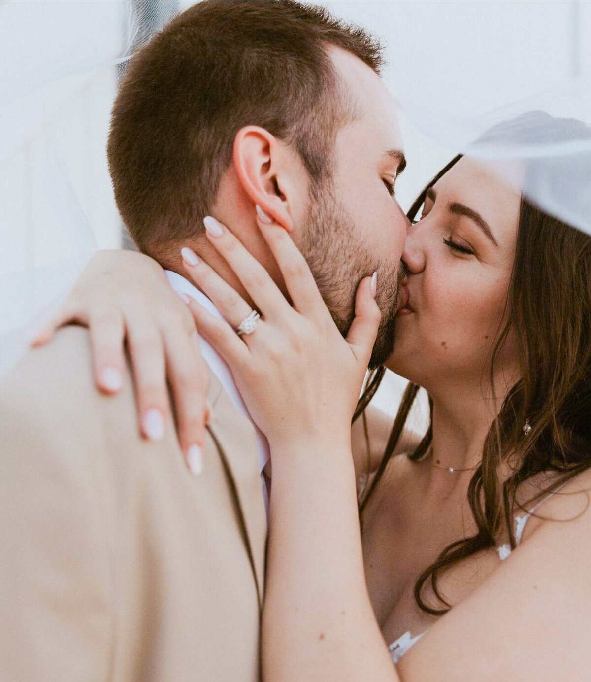 Newlywed couple share a kiss surrounded by veil.