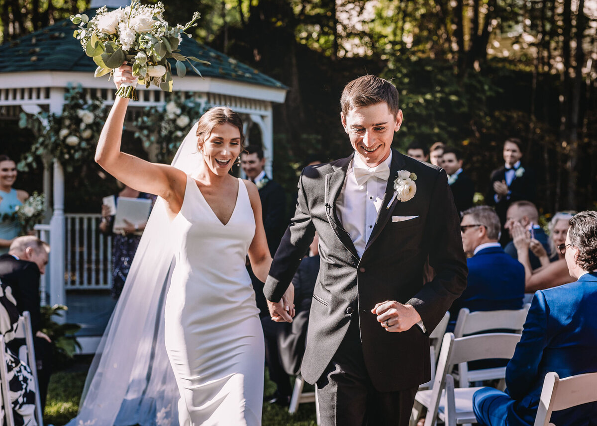 Bride celebrates as her and the groom hold hands and walk down the aisle after ceremony at Wentworth Inn wedding in Jackson NH By Lisa Smith Photography