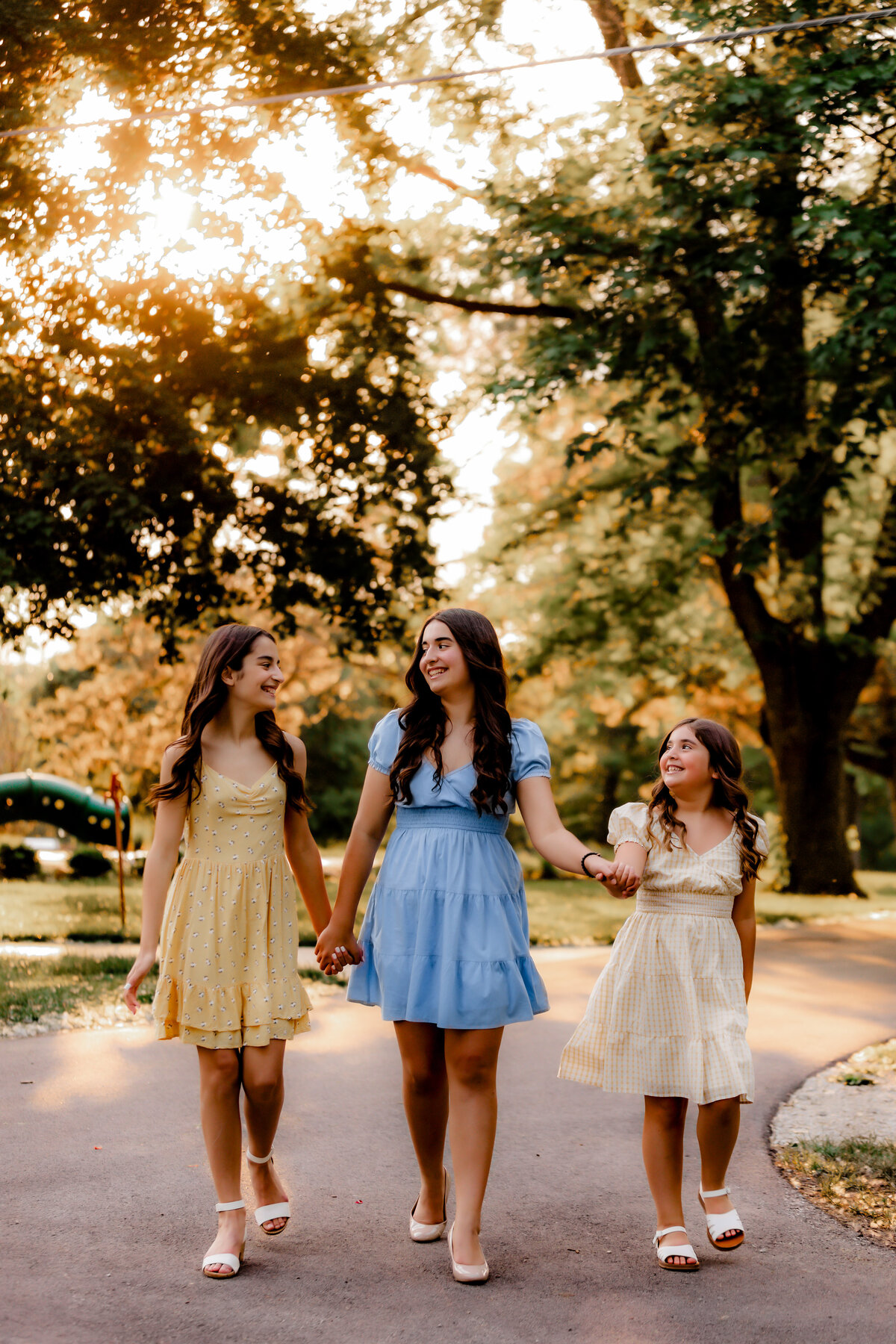 Three girls hold hands and walk down the road.