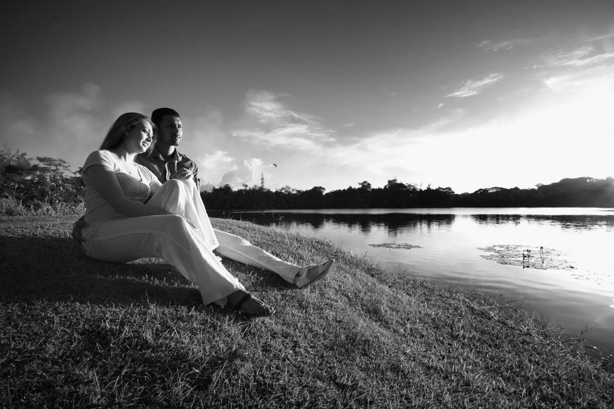 Couple sits on the bank or a lake during the sunset in a B+W capture. Photo by Ross Photography, Trinidad, W.I..