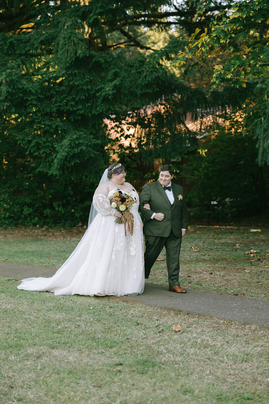 A wedding couple loops arms and walks at their outdoor wedding in Oregon.