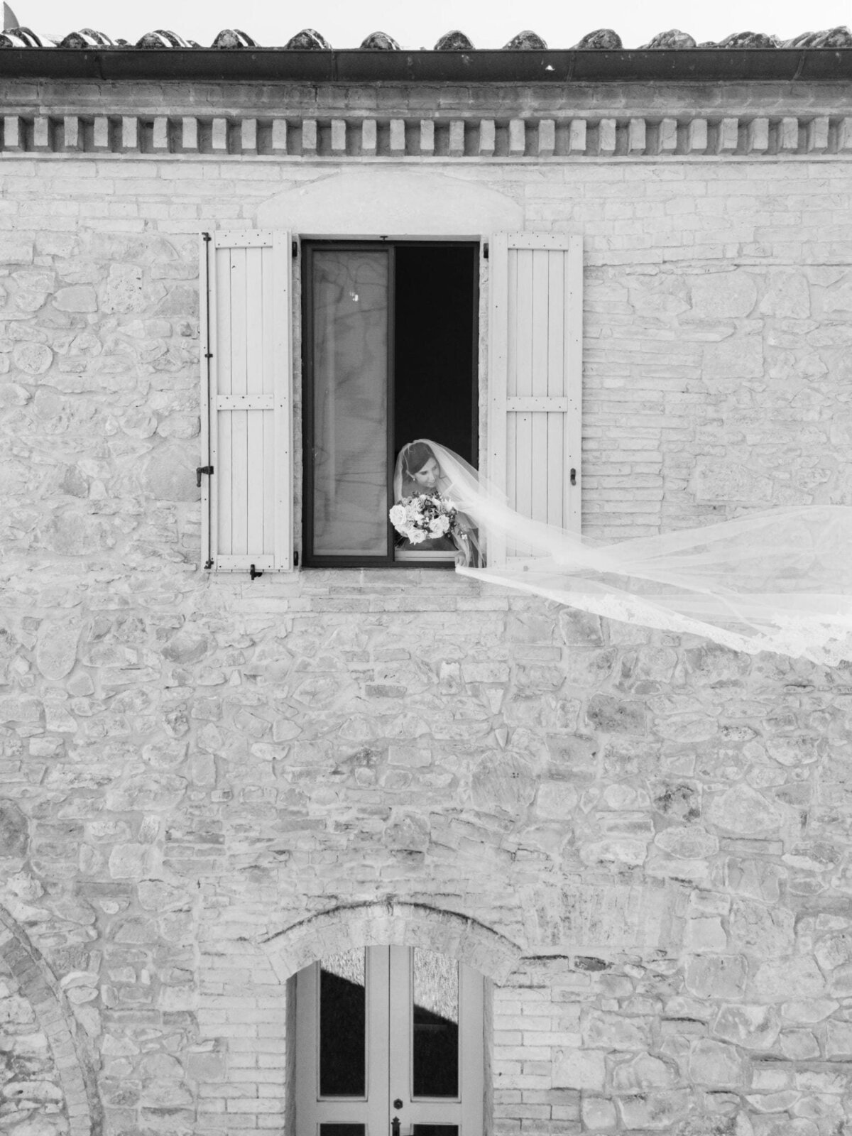 Bride looking outside window with veil flying in the wind during an Ombroneta Wedding in Tuscany