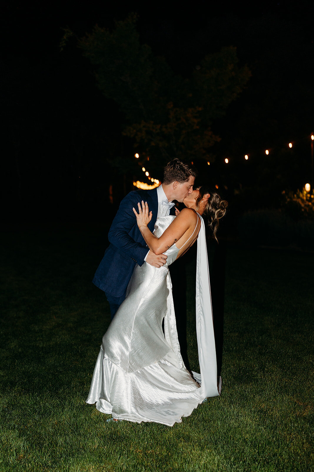 Night portraits with bride and groom sharing  a kiss with fairy lights in the background