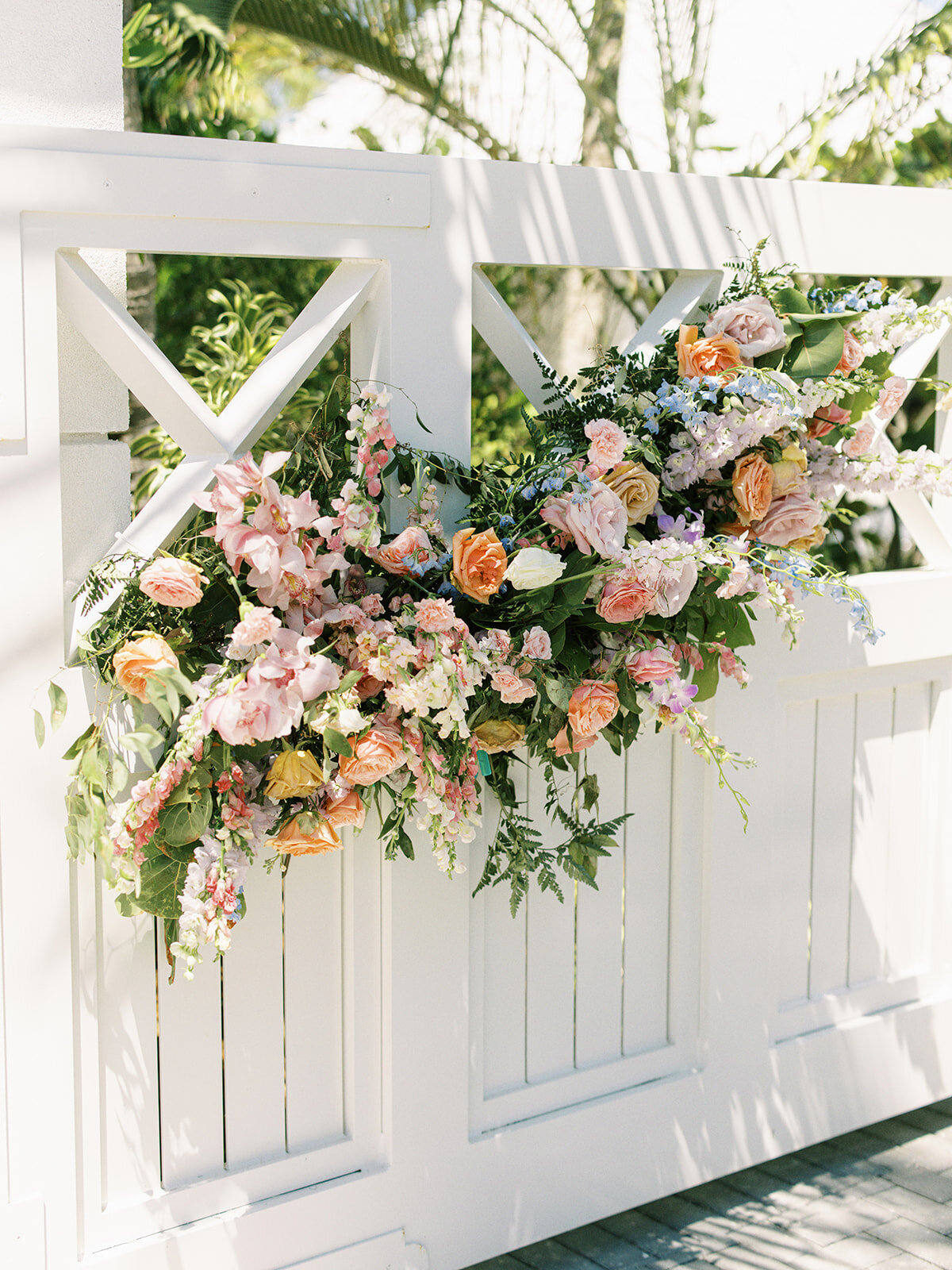 Gate and gatehouse tropical column floral installation for destination spring destination beach wedding in Exuma, Bahamas. Orchids and roses in tropical colors of orange, pink, lavender, dusty blue pale yellow and natural greens. Design by Rosemary & Finch Floral Design.