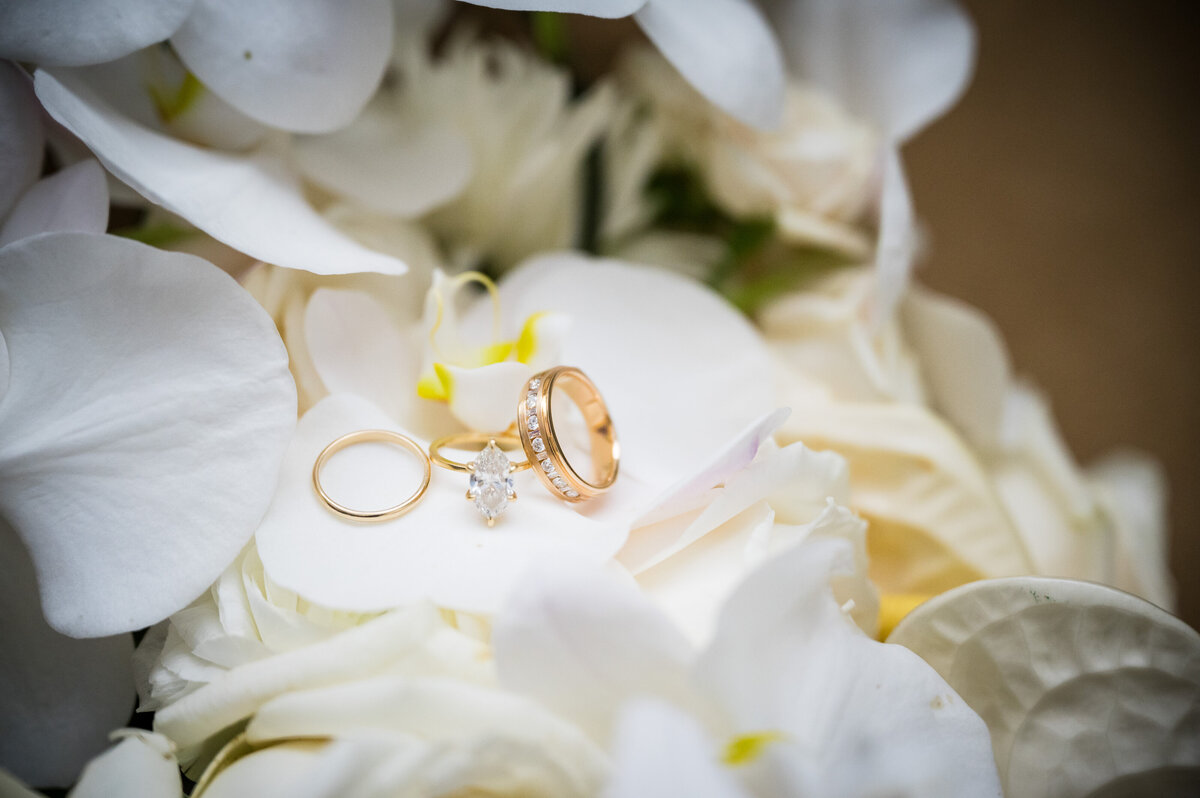 A diamond engagement ring and two gold wedding bands sit on the petals of white flowers, captured by Denver wedding photographer, Casey Van Horn.