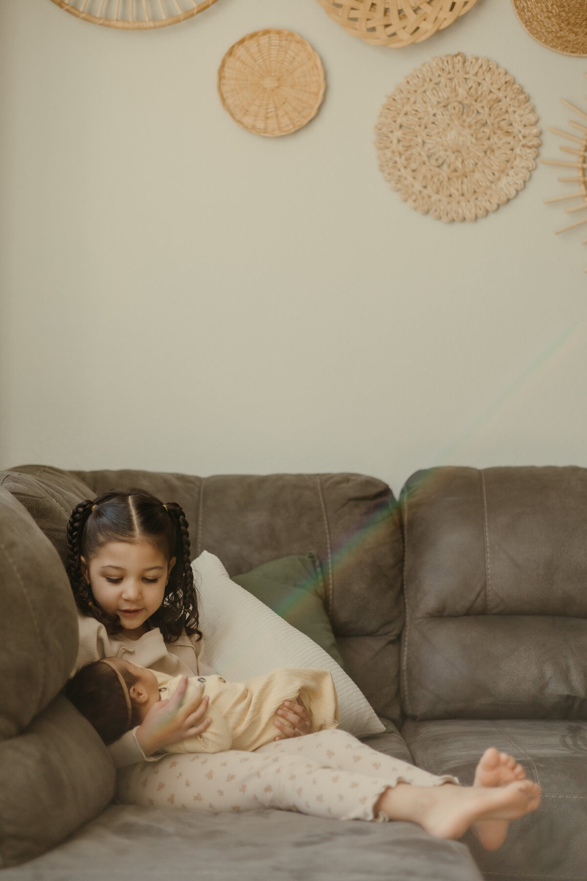 New big sister looking lovingly at newborn baby sister with basket wall in the background in Longmont Colorado