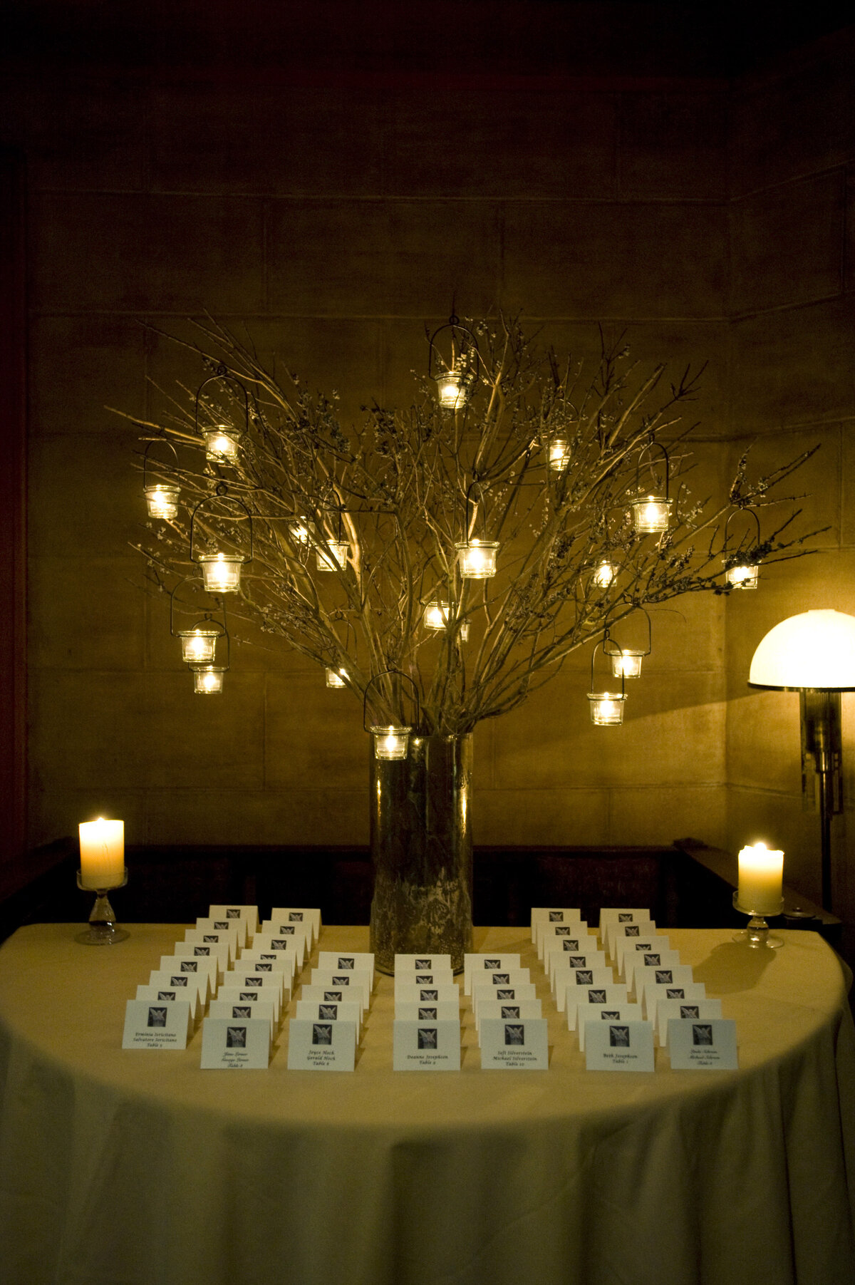 Wedding reception seat assignments on a table with a small tree with hanging candles 