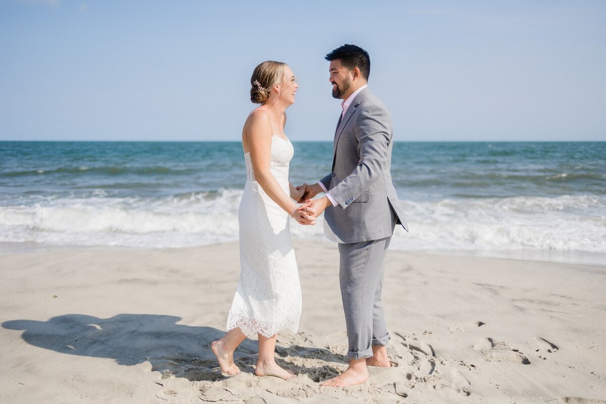 Bride and groom laughing and holding hands at the beach across from the Peter Shields in Cape May