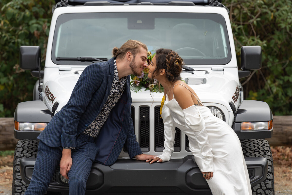 Newlywed leaning across the front of a Jeep about to kiss