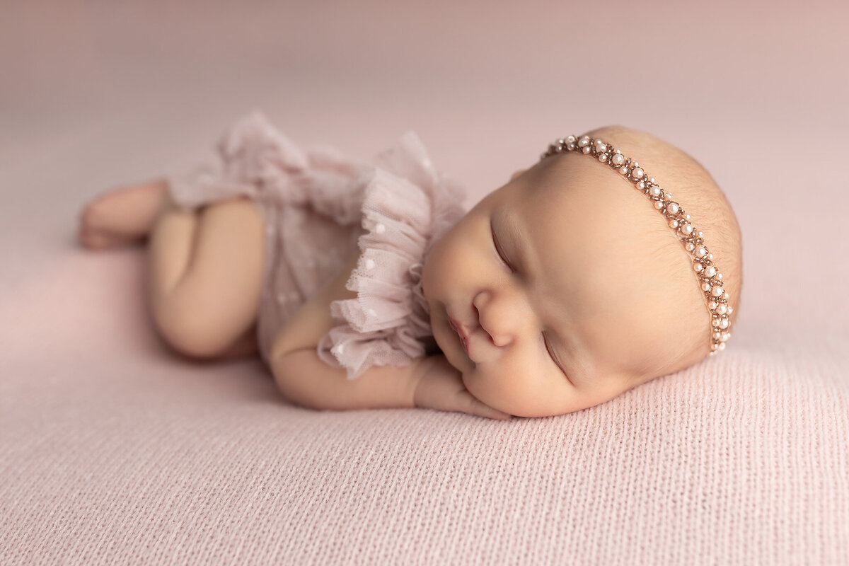 Baby girl peacefully sleeping on a soft pink backdrop in a ruffle romper, perfect for capturing timeless newborn pictures by a baby photographer.