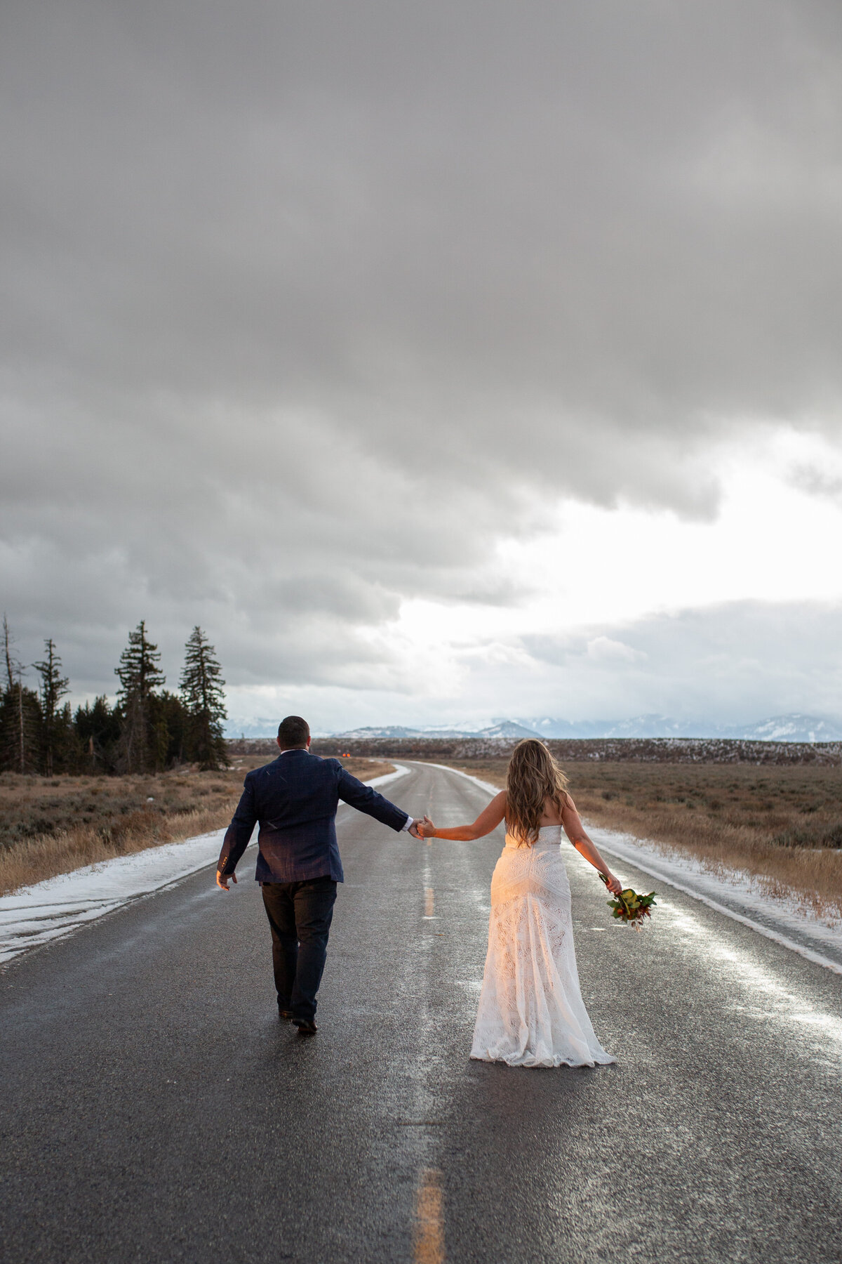 A bride and groom stroll down the road at sunset in Grand Teton National Park.