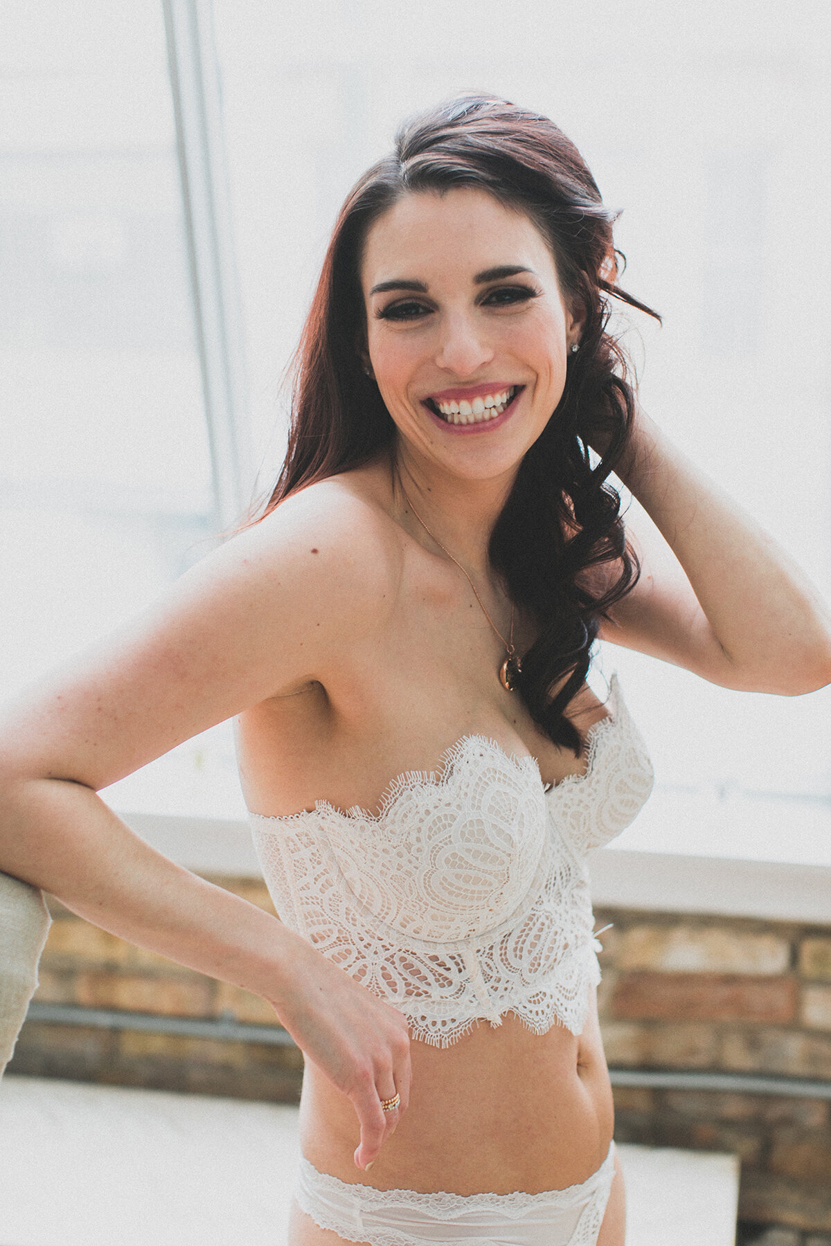 A woman wears all white lingerie and a sentimental necklace for her boudoir photoshoot in Chicago.