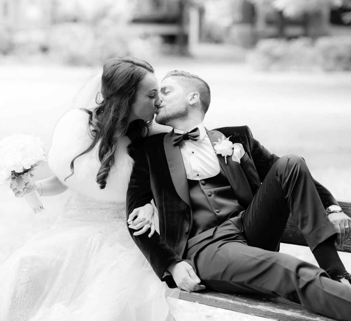 A classic black-and-white image of a bride and groom sitting closely together, sharing a tender kiss, their love beautifully captured in a moment of quiet intimacy.