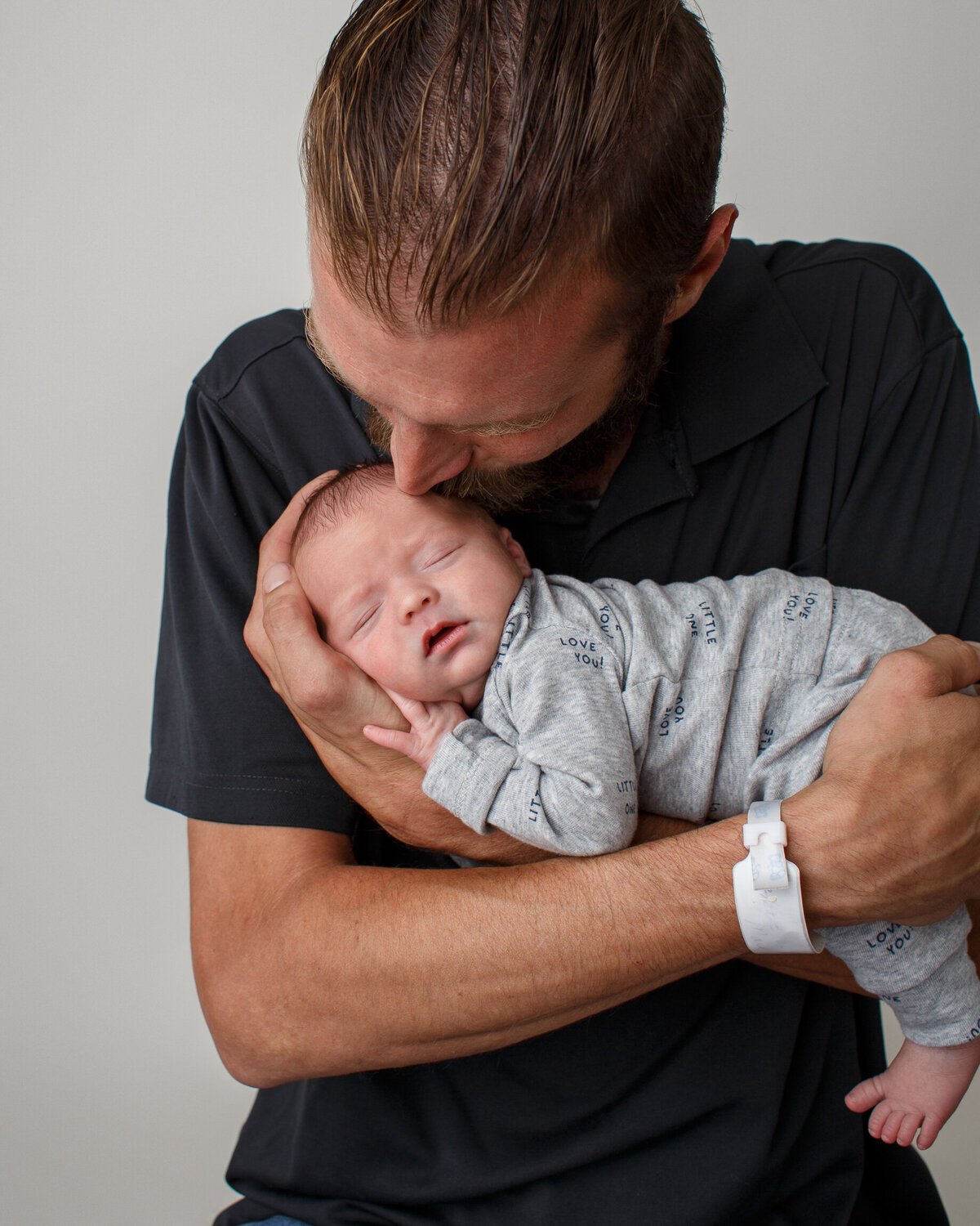Portrait of a father cradling his newborn baby boy in his arms and kissing his head