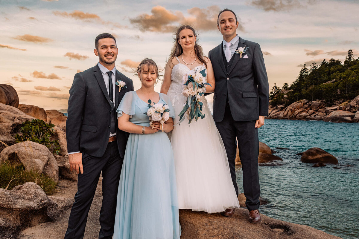 A joyful wedding party poses on rocky cliffs overlooking the ocean, celebrating love against a stunning coastal backdrop. - photo by Jamie Simmons