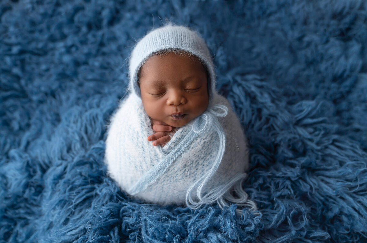 Sleeping baby boy is wrapped in a pale blue swaddle at matching bonnet. His fingers are peeking out from the swaddle in penguin pose. Captured by Bryn Mwar Philadelphia and Main Line photographer Liza Nicole.