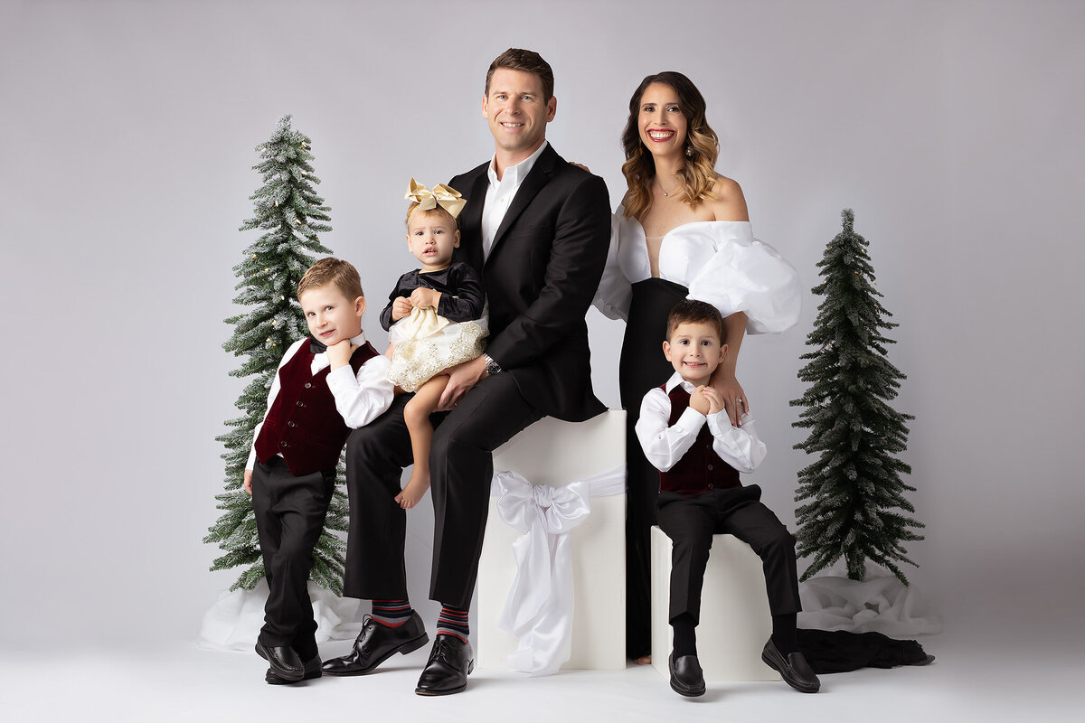 A family posing for a holiday portrait in a festive Dallas family photography session, featuring stylish outfits and winter trees.