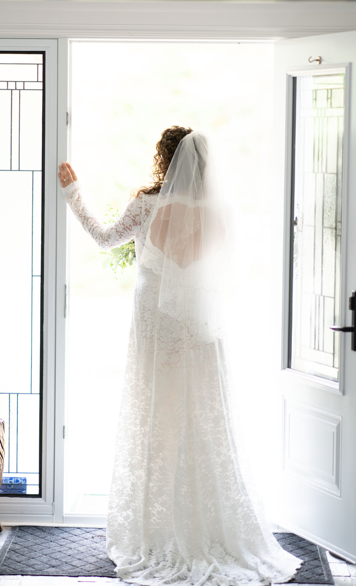 A bride stands gracefully in a doorway, framed by its elegant architectural details. This image captures the bride's poise and the subtle play of light, highlighting her elegant bridal gown and the serene atmosphere of her special day.