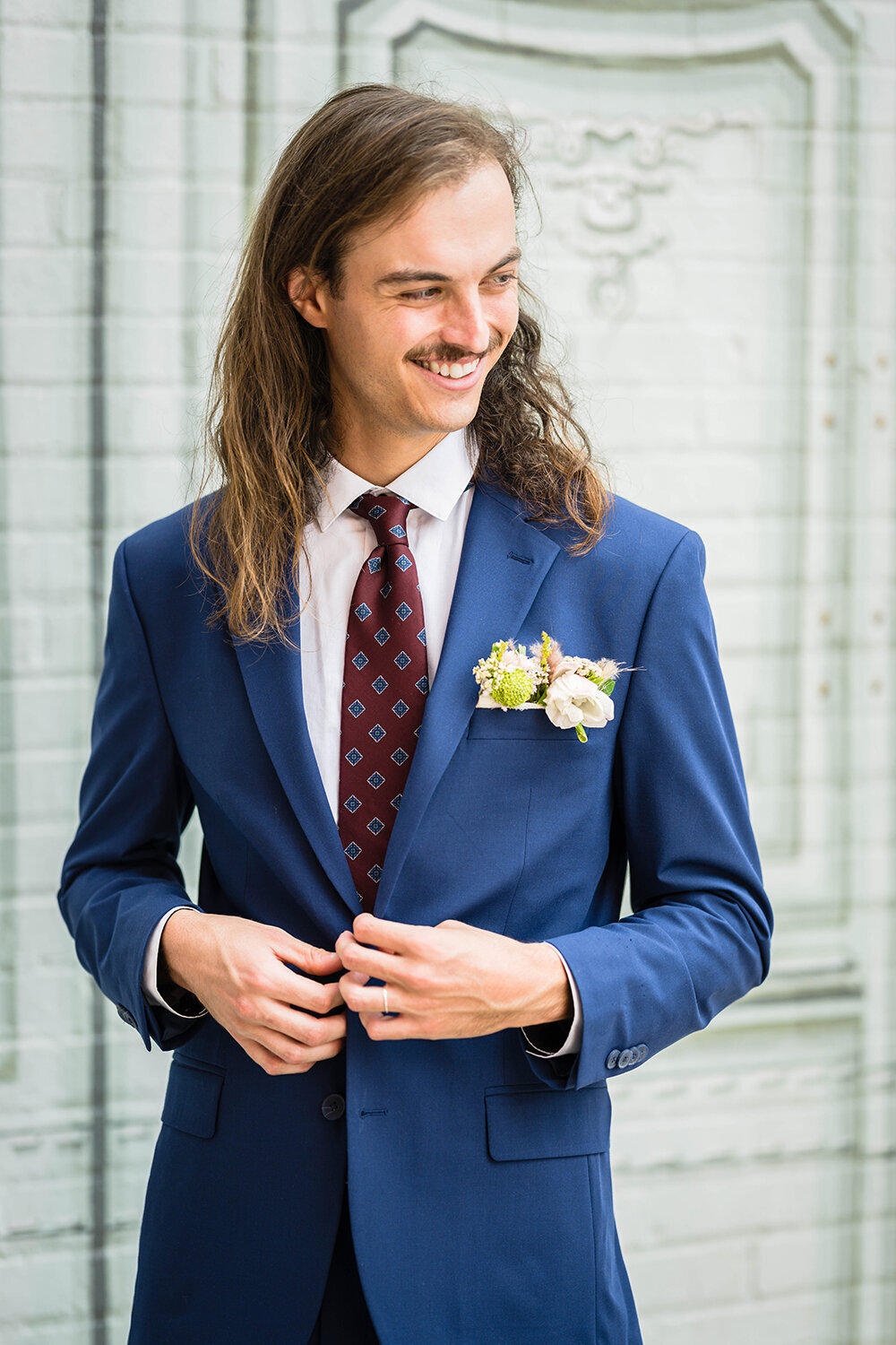 A marrier in a navy suit buttons his top button on his suit jacket and smiles towards something behind the photographer (not photographed) on his elopement day in Roanoke, Virginia.