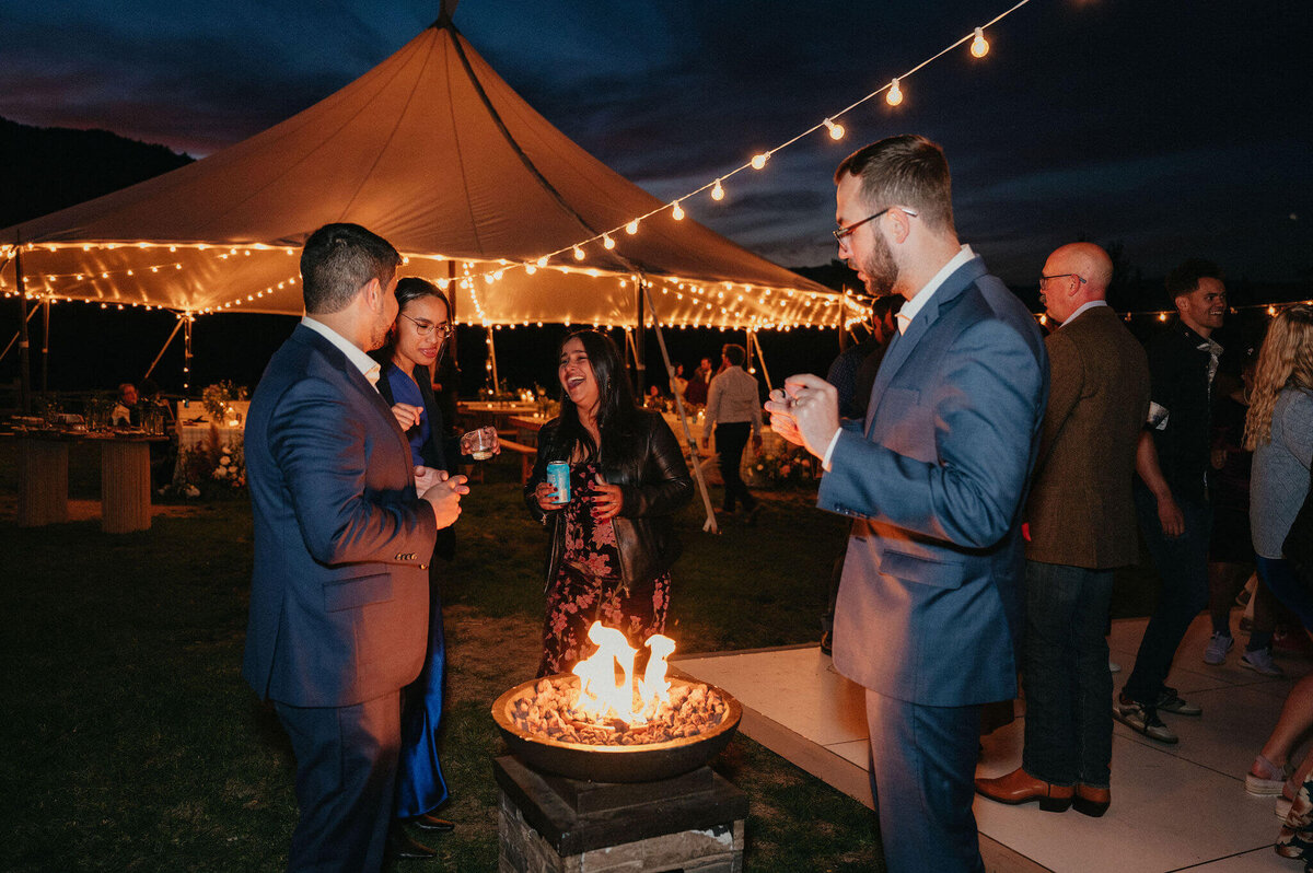 Wedding guests pictured by a fire with stringed lights glowing overhead
